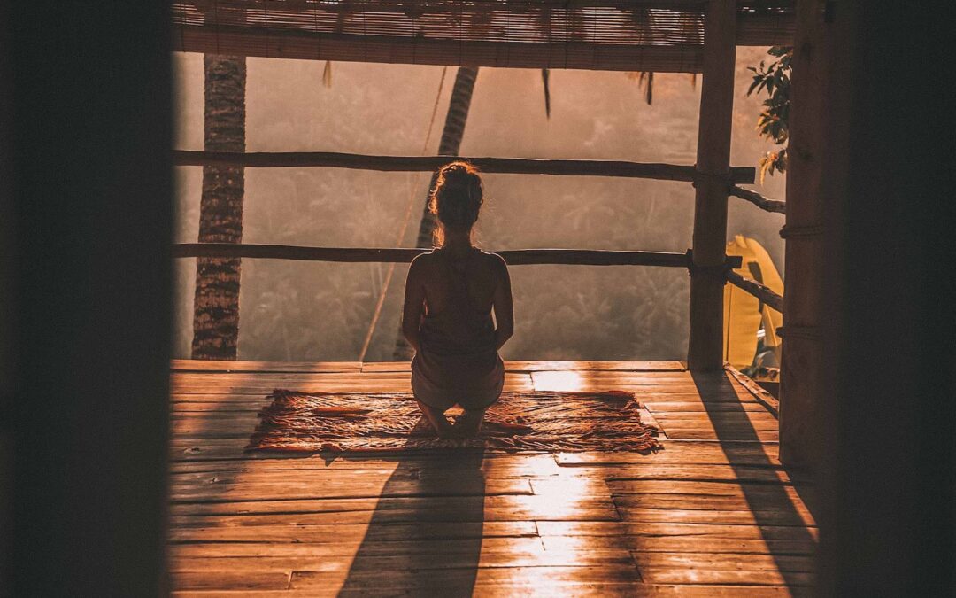 woman meditating on floor with overlooking view of trees